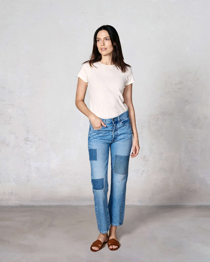 Woman wearing a white t-shirt and blue patchwork jeans against a plain background