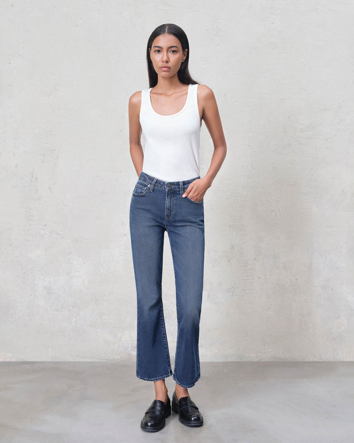 Female model wearing EDWIN jeans mid blue cropped flare with raw hem white tank top and black loafers