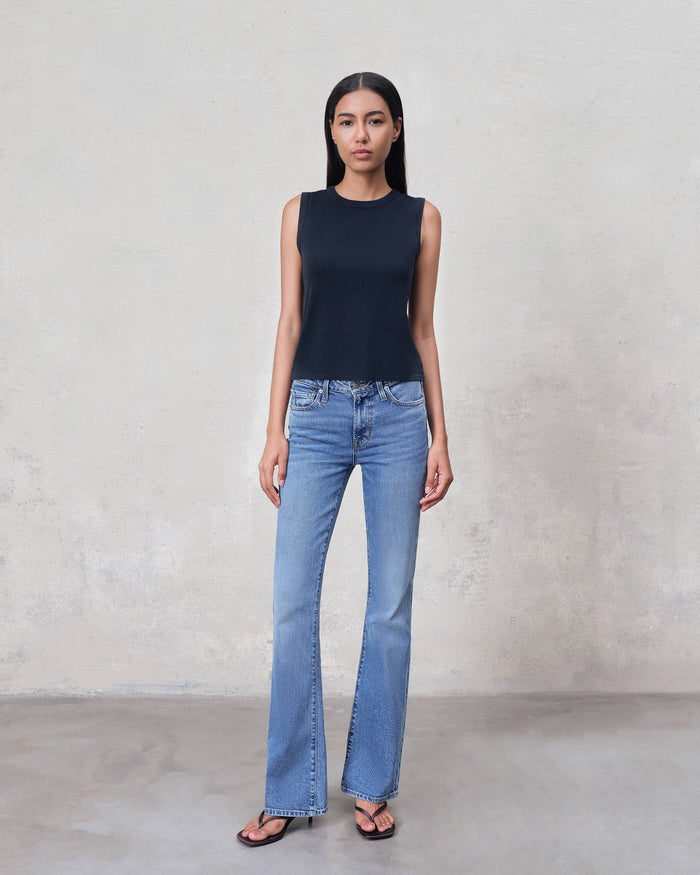 Woman wearing a navy sleeveless top and light blue jeans against a plain background