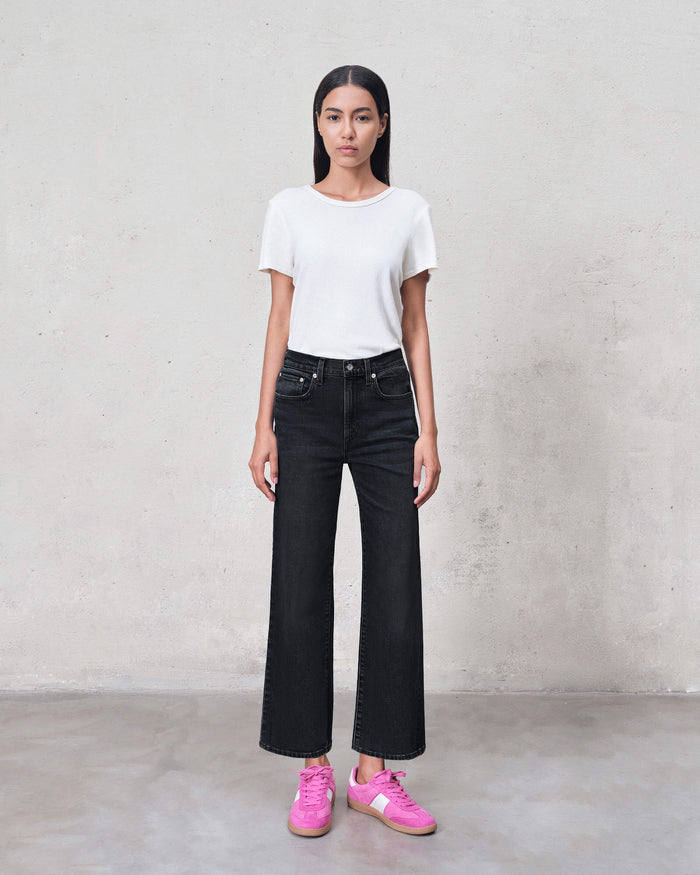 Person wearing a white t-shirt, black jeans, and pink sneakers against a plain background