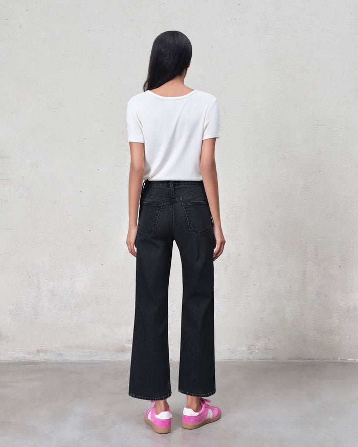 Person wearing black wide-leg jeans and a white shirt against a plain background