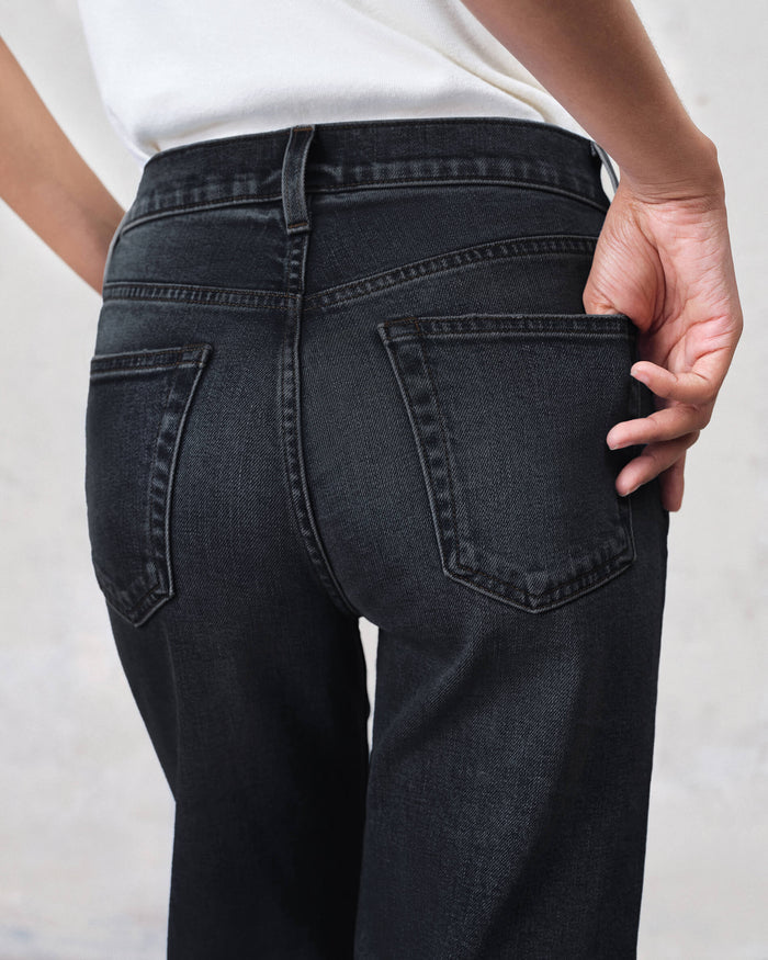 Person wearing dark blue jeans with a plain background