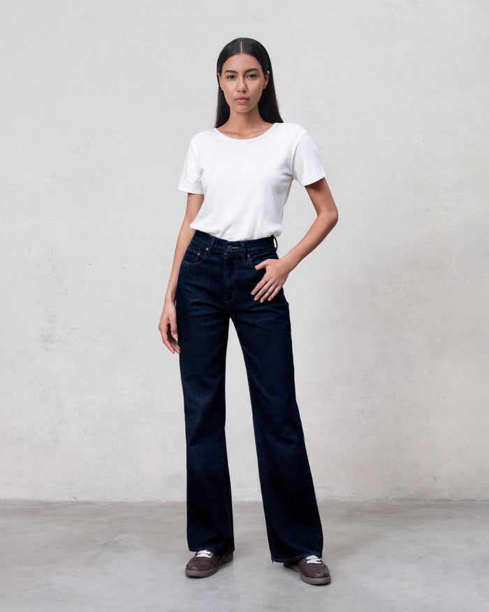 Woman wearing a white t-shirt and dark blue jeans against a plain background