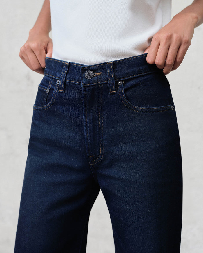 Person wearing dark blue jeans with a plain background
