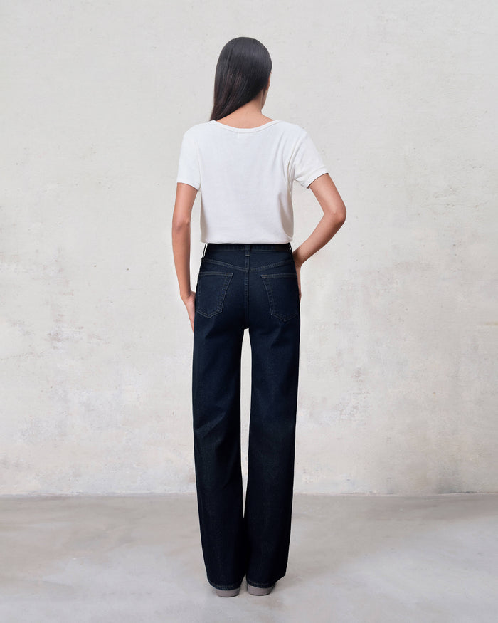 Person wearing a white top and dark blue jeans against a plain background