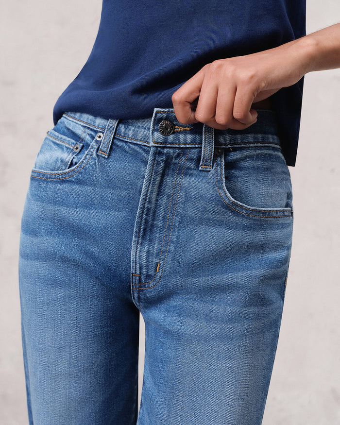 EDWIN light blue high waist jeans closeup with hand fastening button showing wide leg raw hem jeans for women