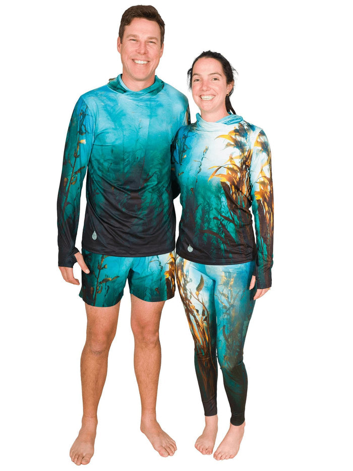 Two people wearing matching teal and black outfits with kelp forest ocean patterns on a plain background