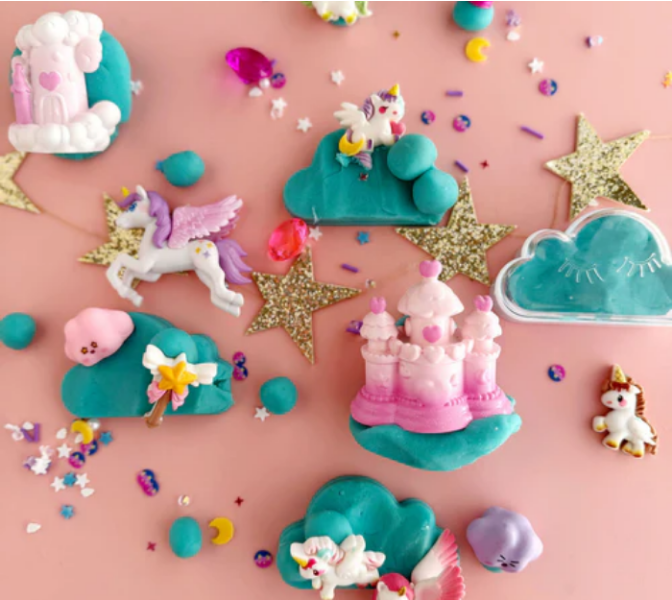 Colorful clay models of unicorns, castles, and clouds on a pink background with stars and confetti.