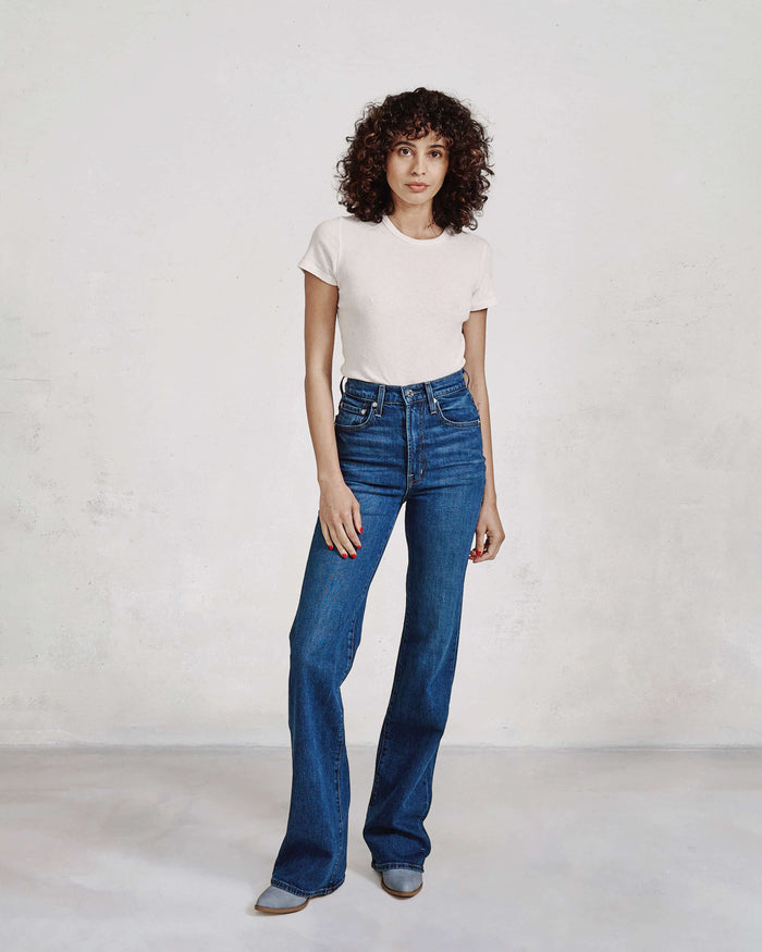 Woman wearing blue jeans and a white t-shirt against a plain background