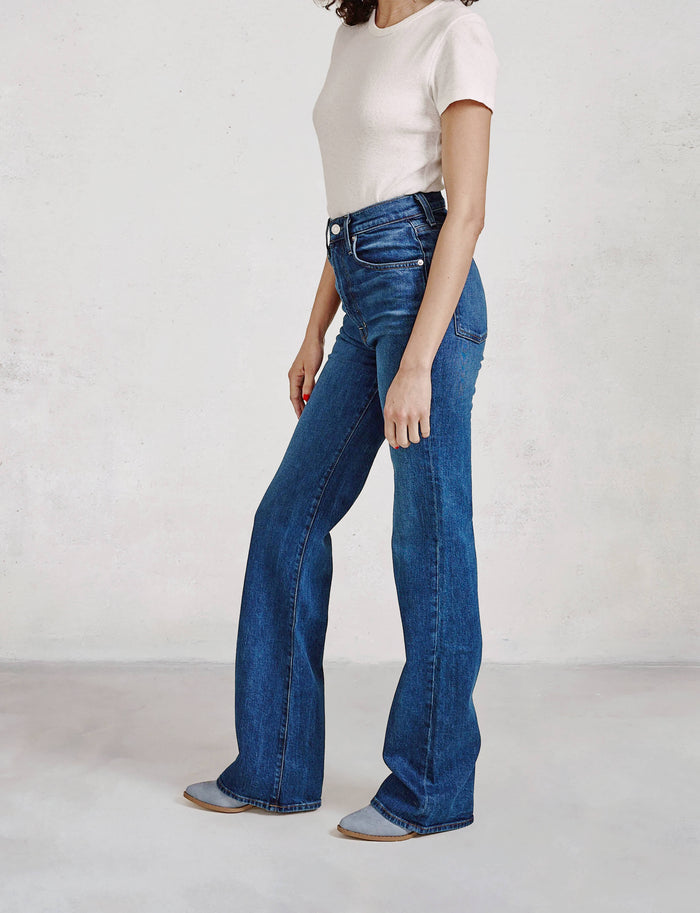 Person wearing blue flared jeans and a white top on a plain background