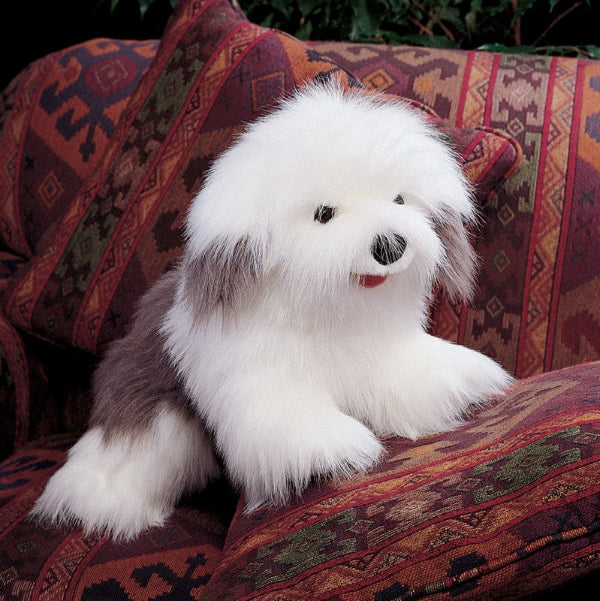 A fluffy sheepdog puppet with a black nose and small red tongue, posed on a patterned armchair.