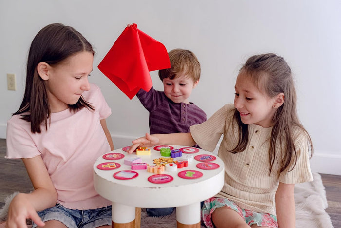 Three children playing with a colorful toy table indoors.