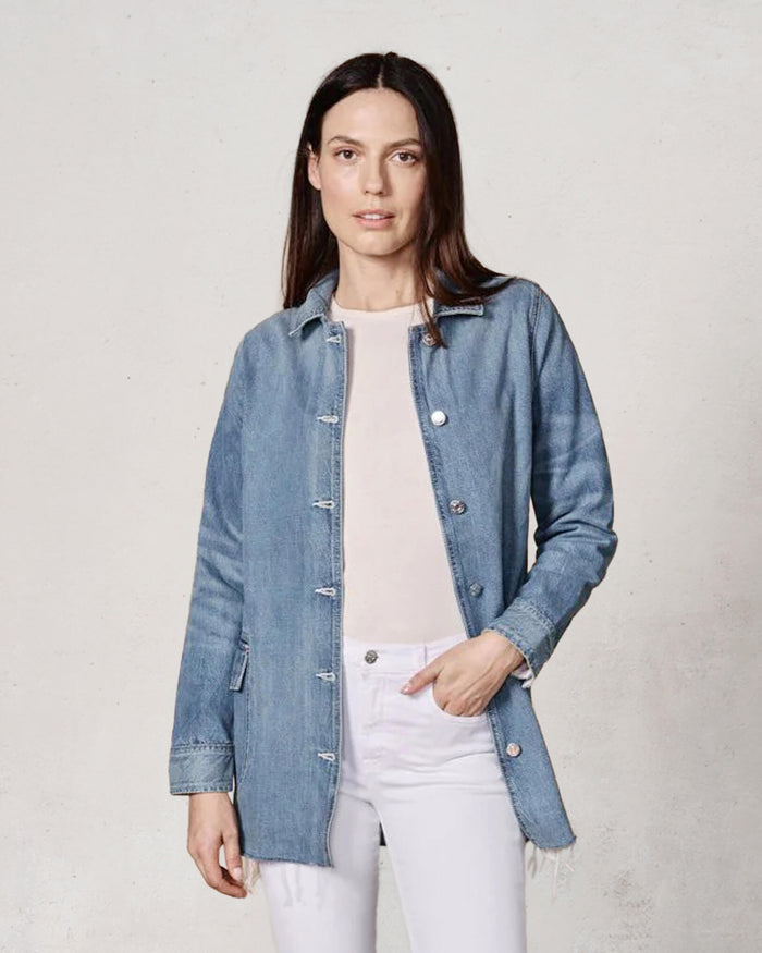 Woman wearing a denim jacket over a white shirt and pants on a plain background
